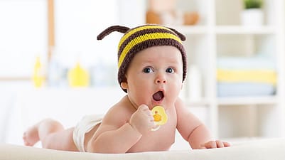 bebé tumbado con un gorrito de abeja y un chupete en la mano