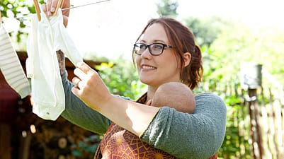 madre tendiendo la ropa mientras lleva a su bebé en porteo