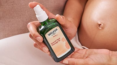 mujer embarazada con un bote de aceite antiestrias de weleda