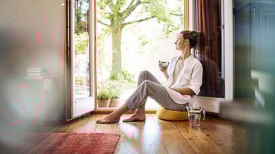 Frau sitzt an der Terrassentuer und trinkt Wasser