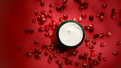 Offener Cremetiegel mit Granatapfelkernen im Hintergrund