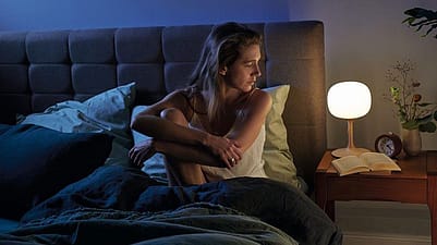Frau im dunklen Schlafzimmer im Bett mit Nachtischlampe an
