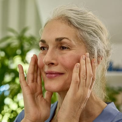 mujer con piel madura echandose crema facial