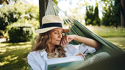 mujer en una hamaca con un libre y un sombrero en la cabeza