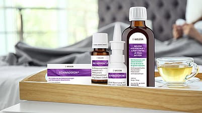 Hustensirup, Infludoron, Echinadoron, Rhinodoron und Fiebermesser auf dem Tisch, Kind schläft im Hintergrund