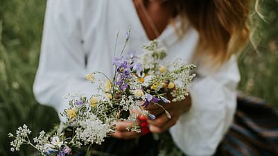 Blumenkranz in den Haenden einer jungen Frau in weissem Hemd