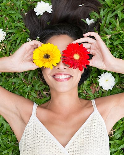Woman lying down on grass with flowers over her eyes