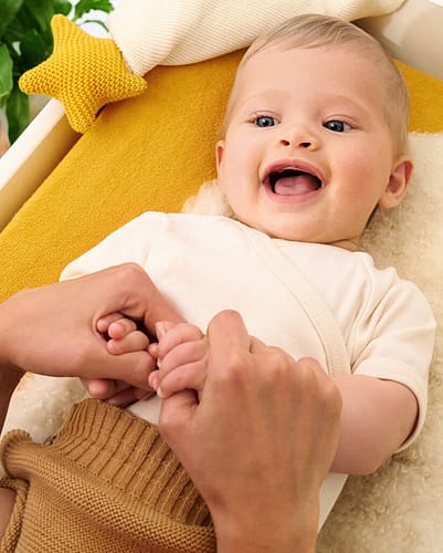 Baby on change mat smiling up at mother