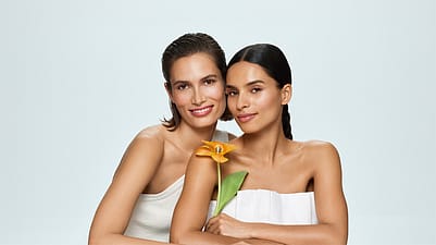 Two women in front of a white background holding a flower
