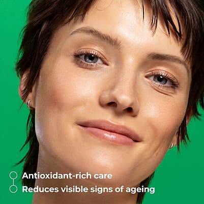A close-up of a woman with radiant, healthy skin against a vibrant green background, highlighting the benefits of antioxidant-rich care and visible reduction of ageing signs.