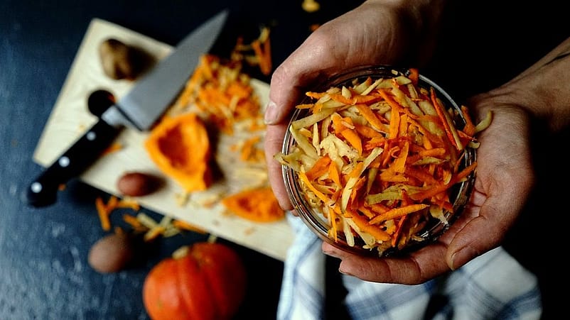 Hand haelt Glasschale mit geraspelten Karotten und Kartoffeln
