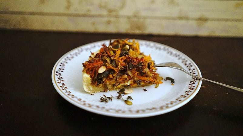 Die fertige Kuerbis-Karotten-Quiche liegt auf einem bemalten Teller mit einer Gabel