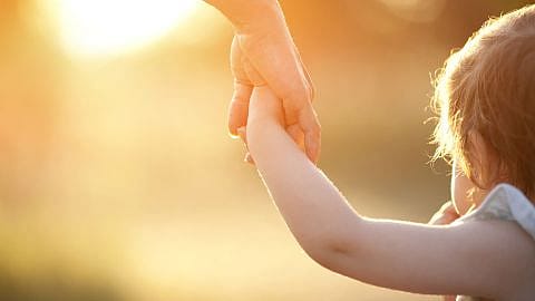 niño dándole la mano a una mujer con el atardecer de fondo