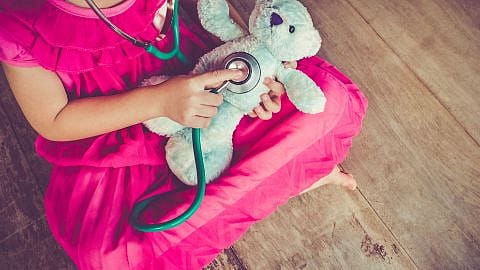 niña sentada en el suelo auscultando a su peluche con un fonendo