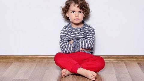 niño enfadado con los brazos cruzados sentado en el suelo