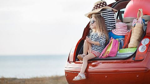 Kind sitzt im geöffneten Kofferraum eines Autos