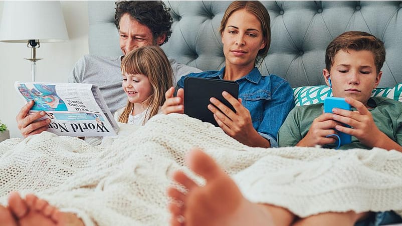 Famille au lit avec des appareils numériques
