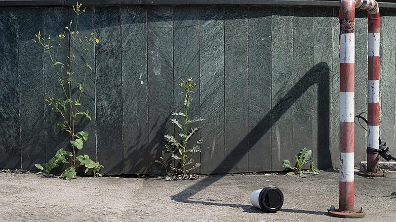 Dettaglio di bordo strada, con un bicchiere a terra e un cordolo a strisce