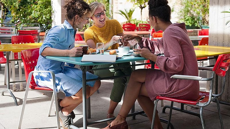 Un gruppo di amiche sorridenti sedute ad un tavolo all'aperto fa colazione