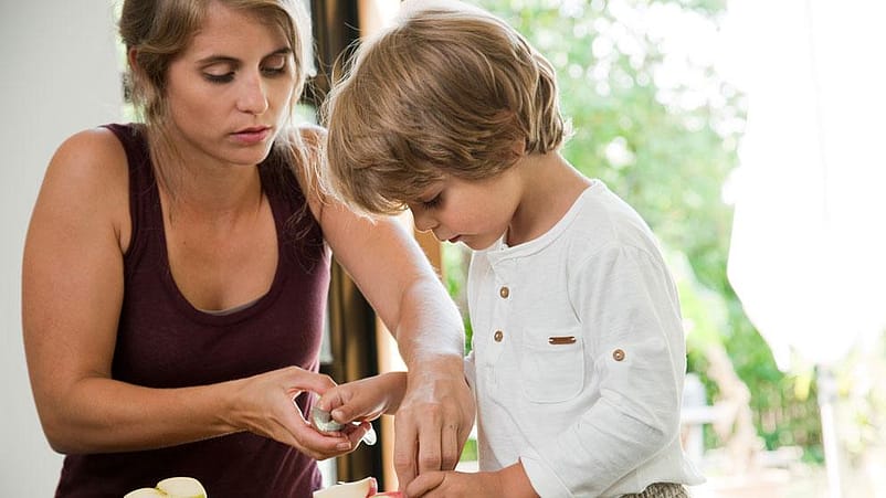 Mujer ayudando a un niño a cortar en trozos una manzana