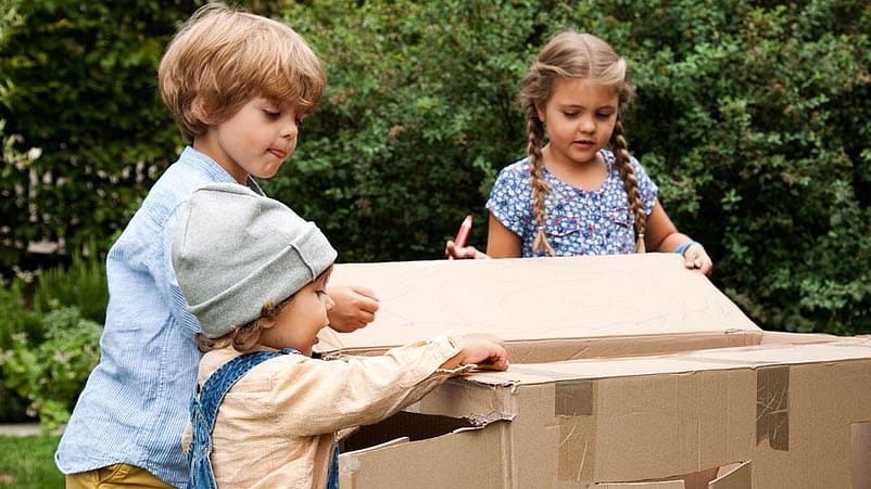 tres niños jugando con una caja de cartón