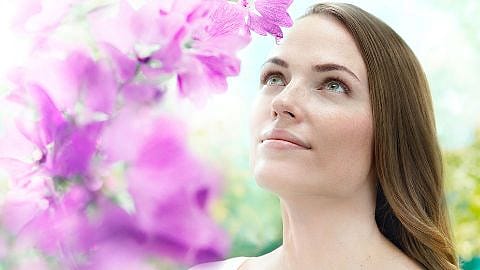 Frau mit Malvenblüten im Hintergrund schaut in den Himmel