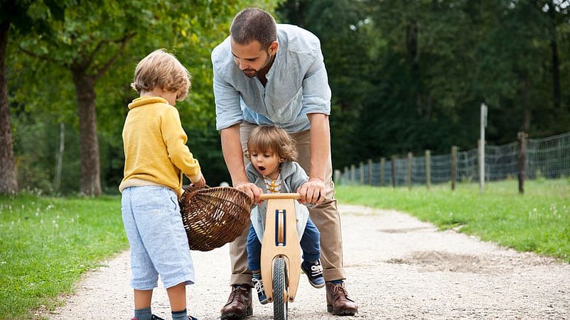 hombre jugando con un niño que tiene una cesta en las manos y otro montado en una bici