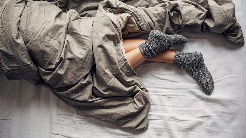 Gambe sotto le coperte e piedi con calzini di cotone in un momento di relax
