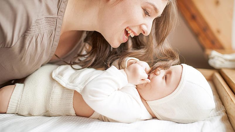 mujer sonriendo observando a un bebé que está tumbado