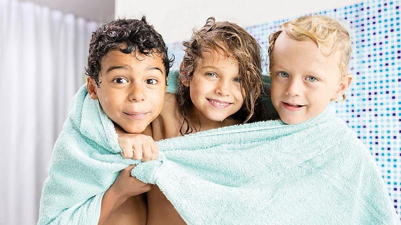 3 niños abrazados sonriendo tapados con una toalla en el baño