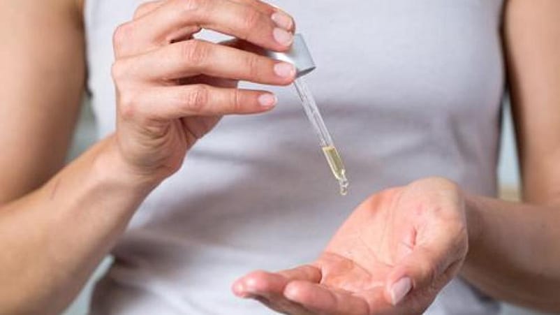 mujer echandose gotas de aceite facial reafirmante desde la pipeta en una mano