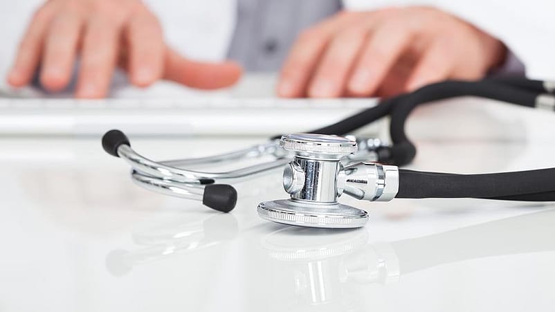 Hände tippen auf einer Tastatur und ein Stethoskop liegt davor