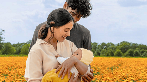 familia formada por un hombre y una mujer abrazando a un bebé en un campo de caléndula