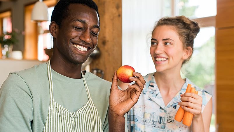 Un ragazzo e una ragazza sorridono mentre tengono in mano frutta e verdura