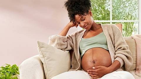 Gravid kvinna sitter i soffan men handen på magen.