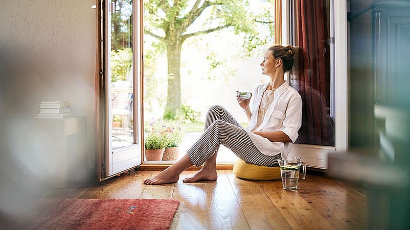 Frau sitzt an der Terrassentuer und trinkt Wasser