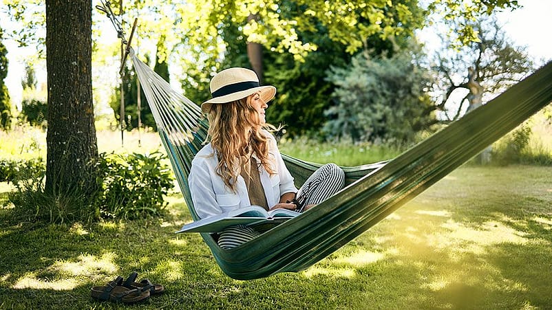 Frau mit Hut liest in der Haengematte ein Buch