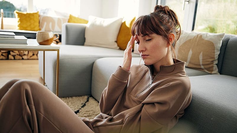 Frau sitzt im Wohnzimmer am Boden und lehnt an die Couch