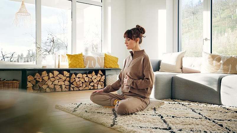 Frau sitzt im Schneidersitz am Boden und hält sich den Bauch