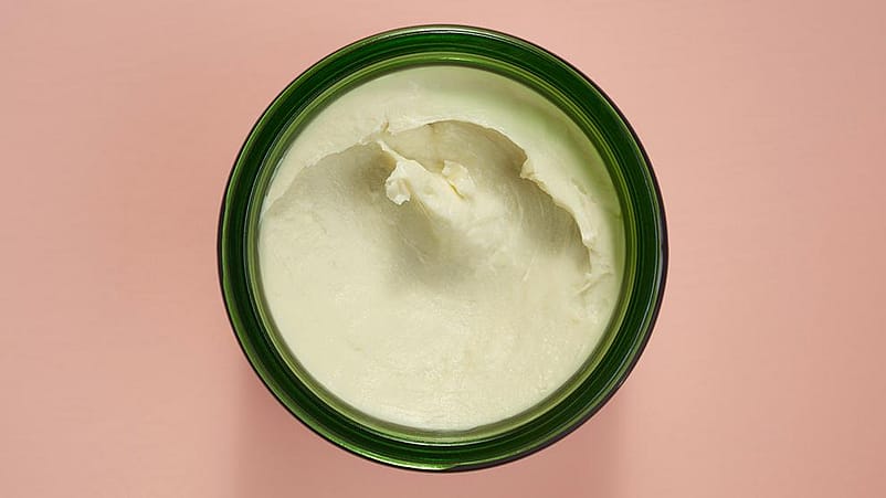 overhead shot of open jar of body butter with pink background