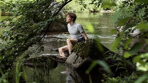 Mann sitzt auf einem Stein im See
