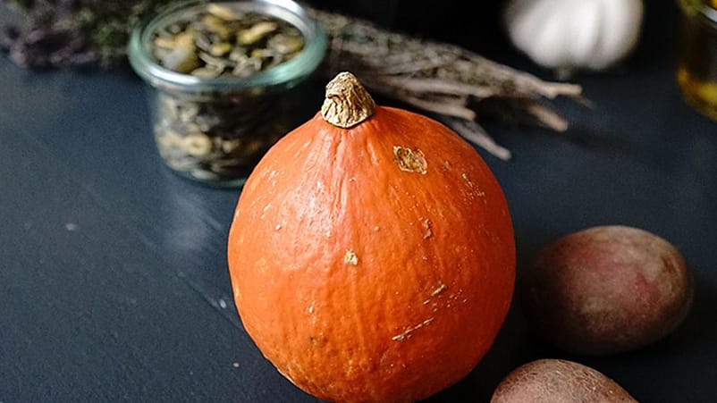 Auf einem Tisch liegen ein Hokkaidokuerbis und eine Glasschalen mit Kuerbiskernen