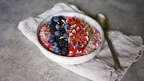 Bowl mit Muesli garniert mit frischen Brombeeren, Heidelbeeren, Feigen und Saaten