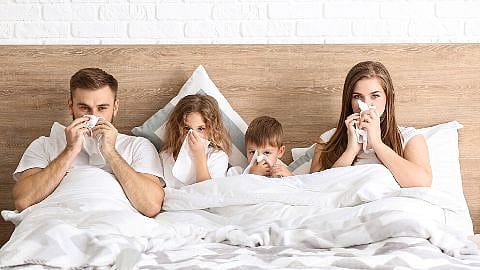 Familie im Bett alle schneuzen sich
