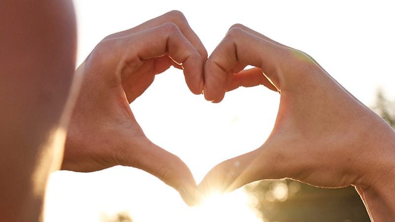 mujer haciendo un corazon con los dedos en una puesta de sol