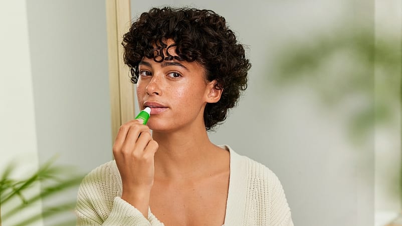 Une femme met du baume à lèvres Skin Food sur ses lèvres
