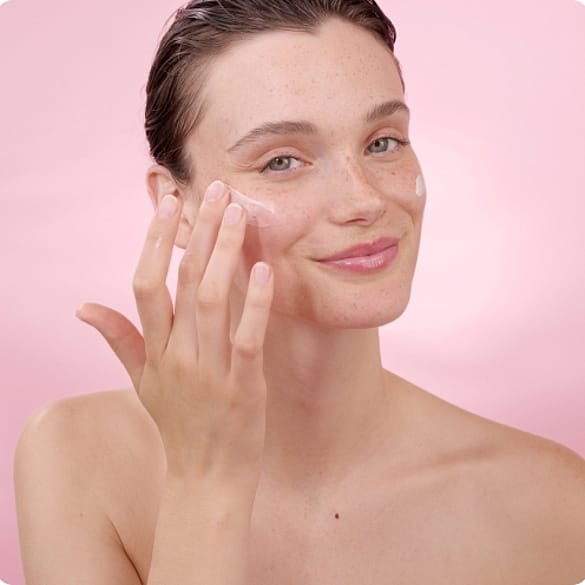 Junge Frau trägt weiße Creme auf ihre Haut auf