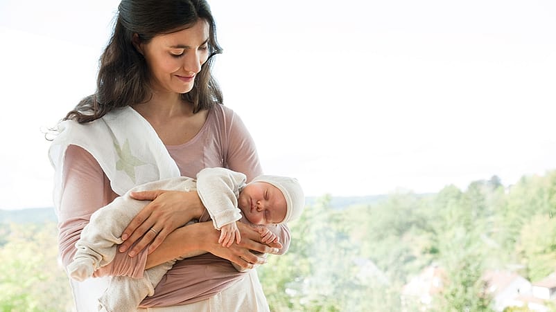 mujer mirando y sonriendo al bebé que tiene cogido en brazos