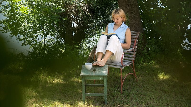 kvinna sitter på en stol vid vattnen och läser en bok