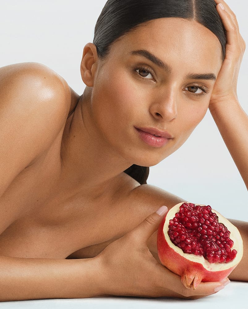 Frau stützt liegend ihren Kopf in die Hand und hält einen Granatapfel